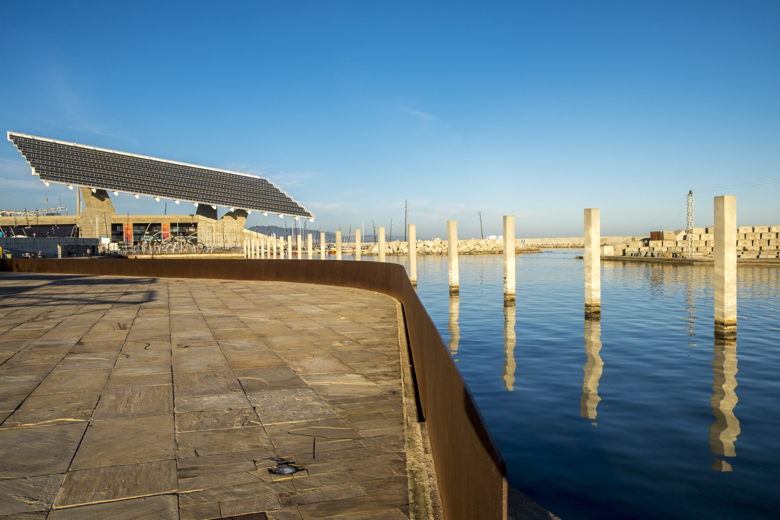 Vista panorâmica de uma estrutura metálica imponente no cais, com céu azul e água ao fundo, destacando a durabilidade do aço nas construções externas.