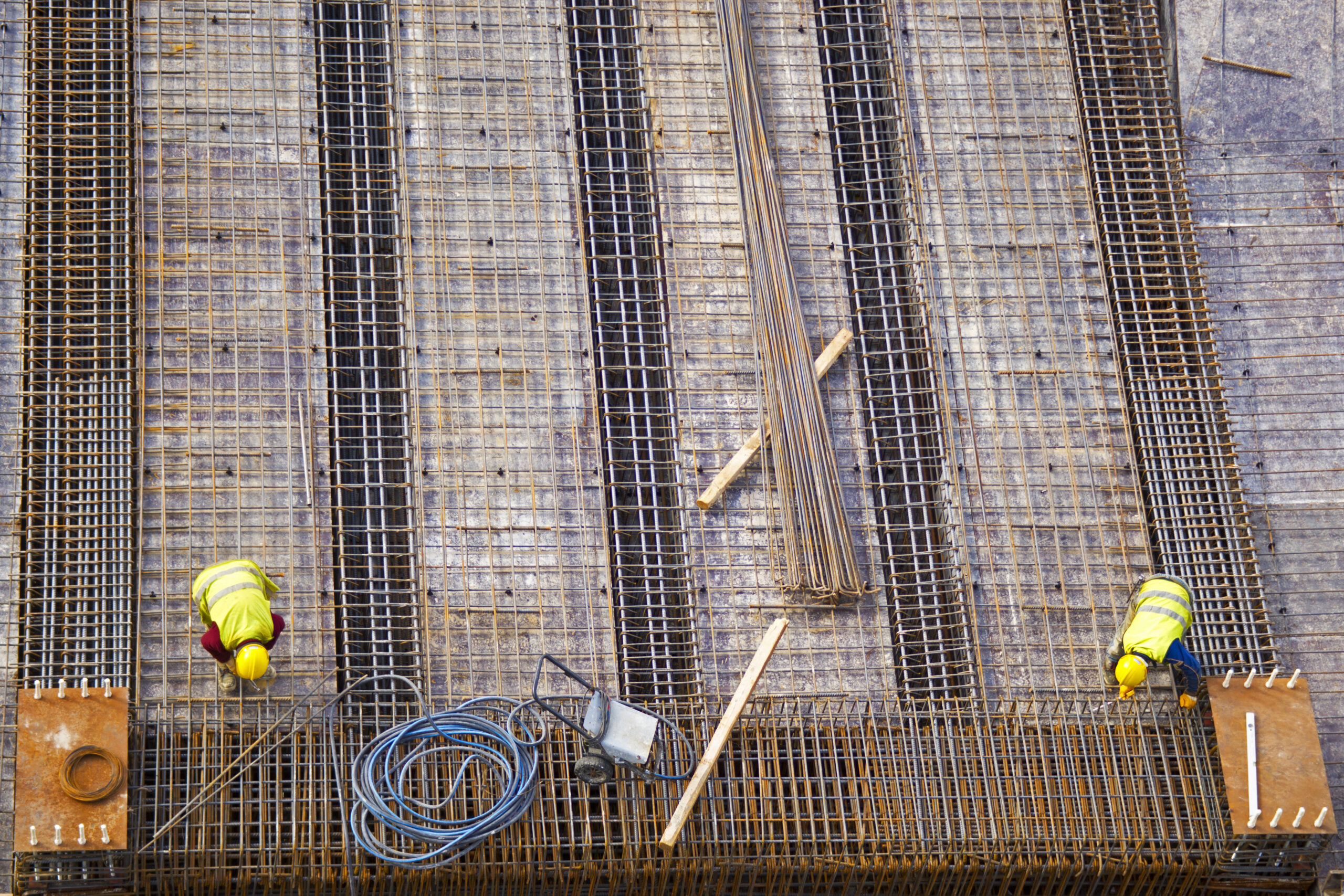 Dois trabalhadores montando barras de aço e estrutura metálica em um canteiro de obras, representando a construção de uma estrutura sólida.